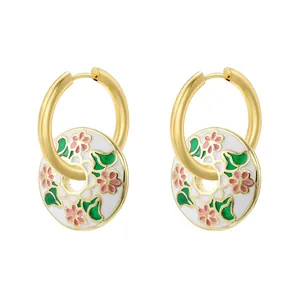 Close-up of gold hoop earrings with white enamel floral charms and green leaves