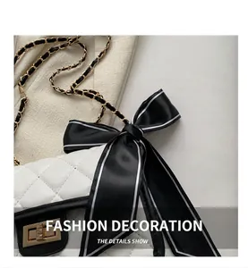 Close-up of white quilted chain bag featuring a black silk bow and gold metal lock
