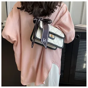 Detail of white quilted crossbody bag with black trim and elegant ribbon bow accent