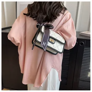 Detail of white quilted crossbody bag with golden clasp and decorative silk scarf