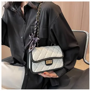 Detail of white quilted handbag with black trim, gold clasp and scarf-wrapped chain