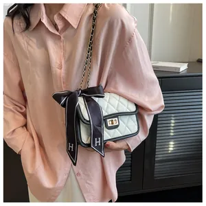 Close-up of white quilted crossbody bag with gold clasp and black ribbon with H logo