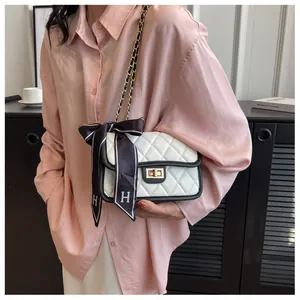 Detail of white quilted crossbody bag with gold twist lock and a silk scarf tied to the chain