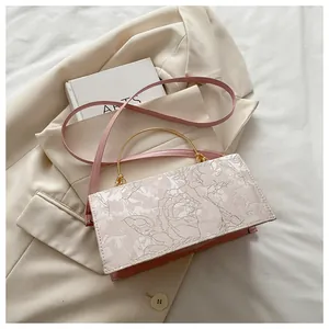 Close-up of pink leather shoulder bag featuring floral embroidery and gold metal handle
