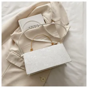 Macro detail of white square bag featuring floral embossed texture and gold handle