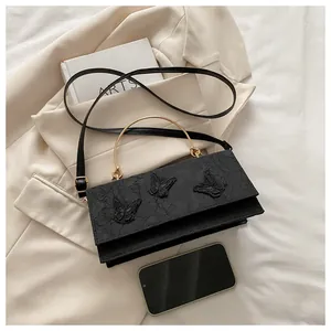 Close-up of black crossbody bag with 3D butterfly embroidery and gold metal handle