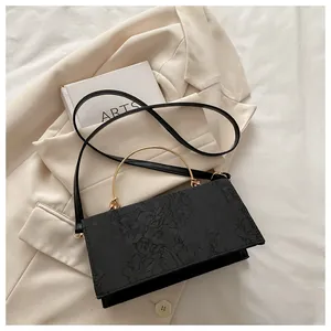 Detail of black rectangular crossbody bag with 3D floral relief and gold metal handle