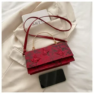 Detail of red fabric rectangular bag with butterfly embroidery and golden ring handle