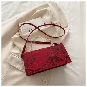 Detail of red floral lace handbag with curved gold metal handle and long shoulder strap