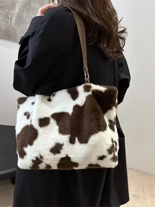 Plüsch-Schultertasche mit braunem Kuhmuster und Lederriemen am Modell gezeigt