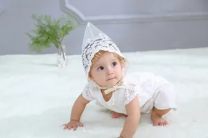 Close-up of white lace baby bodysuit and matching pointed bonnet on a plush carpet