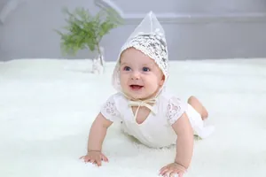 Detailed close-up of baby girl lace romper and pointed bonnet on soft plush carpet