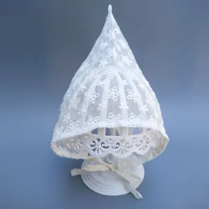 Detail of white lace baby bonnet featuring floral embroidery and scalloped ribbon ties
