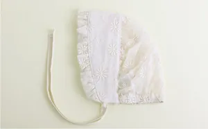 Detailed macro view of white baby bonnet with floral lace embroidery and ruffled edges