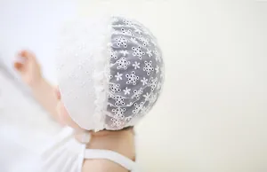 Close-up of white lace baby bonnet with star and flower embroidery and ruffled edges