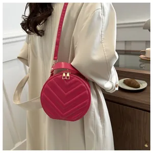 Detail of a round quilted crossbody bag in vibrant fuchsia with a top handle and strap