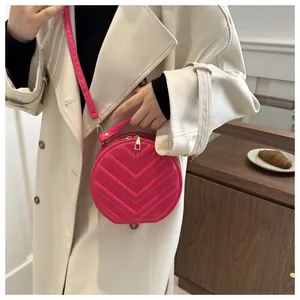 Close-up of bright pink round crossbody bag with V-shaped quilting on a beige trench coat