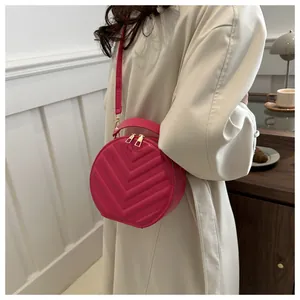 Detailed view of a bright pink round crossbody bag with chevron quilting and gold zippers