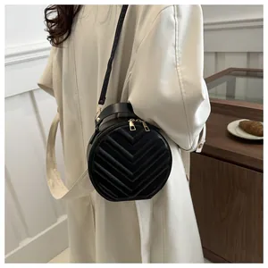 Detail of black round crossbody bag with V-shaped quilted texture and gold zipper