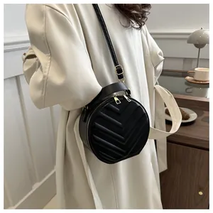 Detail of black round crossbody bag featuring V-shaped quilting and gold zippers