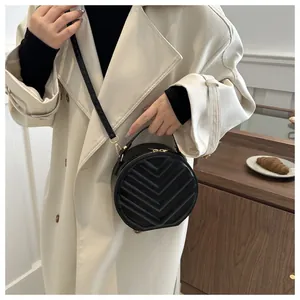 Detail of a black quilted round crossbody bag with gold zippers worn with a beige coat