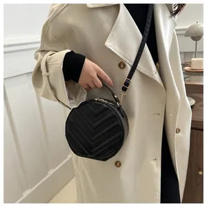 Detail of black chevron quilted round crossbody bag styled with a cream trench coat