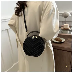 Detail of round black quilted crossbody bag with golden dual zippers and leather handle
