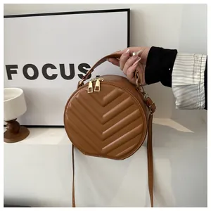 Detail of a brown circular crossbody bag with V-shaped quilting and golden zippers