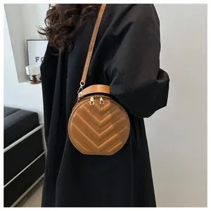 Model wearing a round brown crossbody bag with V-quilted texture and top handle