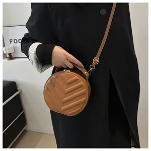 Detail of brown quilted round crossbody bag featuring golden hardware and leather strap