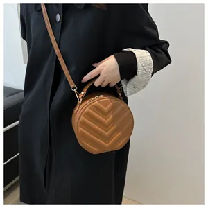 Detail of a brown quilted round crossbody bag shown on a model wearing a black coat