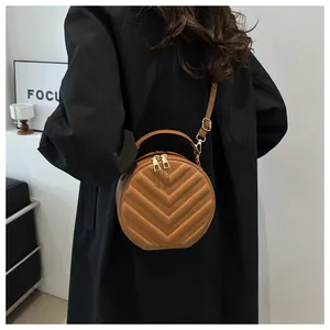 Close-up of a brown circular crossbody bag with chevron quilting and golden hardware