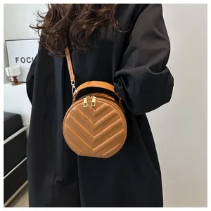 Detail shot of brown round crossbody bag with V-shaped stitching and gold zippers