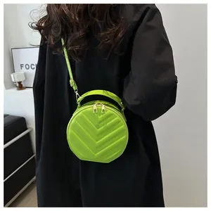 Neon green round crossbody bag with chevron stitching shown on model in black shirt