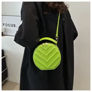 Detail of bright green round crossbody bag with chevron quilting worn over black coat