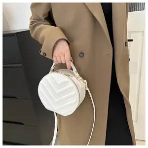 Close-up of white round quilted crossbody bag with V-shaped stitching and gold zipper