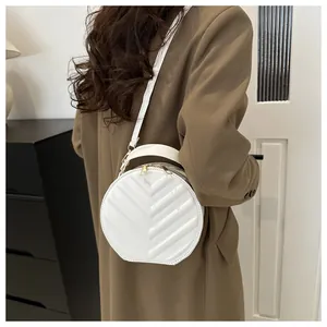 White round quilted crossbody bag with golden zippers worn over a brown coat