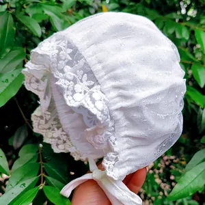 Close-up of white lace baby bonnet with detailed floral embroidery and silk ties