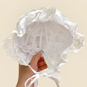 Detail of baby lace bonnet featuring delicate white floral embroidery and scalloped edges