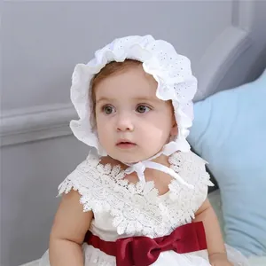 Detailed close-up of white lace baby bonnet and dress with a dark red silk bow accent