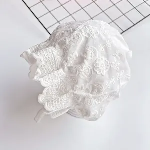 Macro detail of intricate white lace flower embroidery on a summer baby bonnet