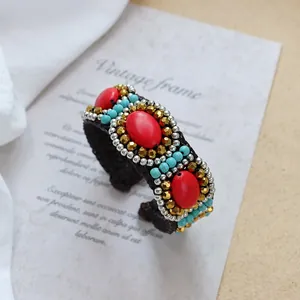 Detail of bohemian woven cuff with red oval stone and blue beads on vintage background