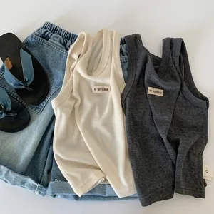 Flat lay of cream and charcoal waffle knit vests for kids with a small chest patch