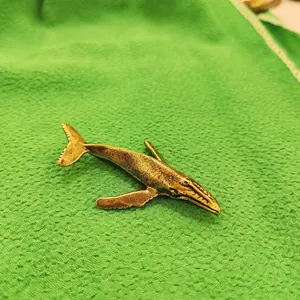 Macro shot of an antique brass whale pin with a textured finish on green fabric