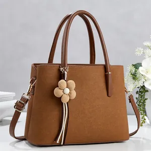 Brown litchi texture tote bag with top handle and floral pendant on marble surface