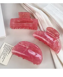 Primo piano di tre mollette per capelli in acrilico rosa marmorizzato su seta bianca