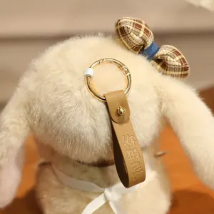 Macro shot of khaki plush rabbit pendant featuring gold key ring and leather strap details