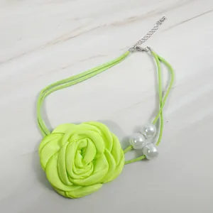 Detail of neon green fabric rose choker with white pearls on a marble surface