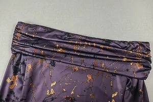Détail de tissu froncé violet foncé avec imprimé floral doré et texture soyeuse