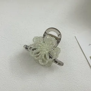 Detail view of woven flower hair claw with iridescent pearls on grey plastic base